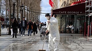 A masked worker wipes the pavement of the Champs Elysees avenue in Paris, Friday, March 13, 2020.