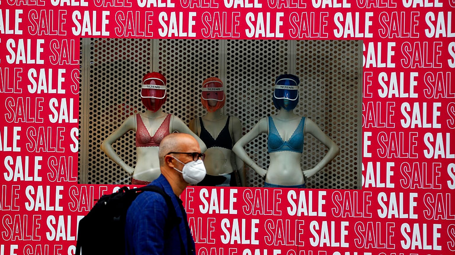 A man wearing a protective face mask walks past a shop window in London