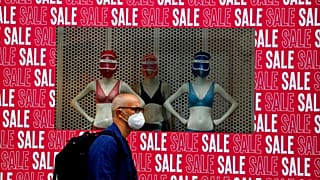 A man wearing a protective face mask walks past a shop window in London