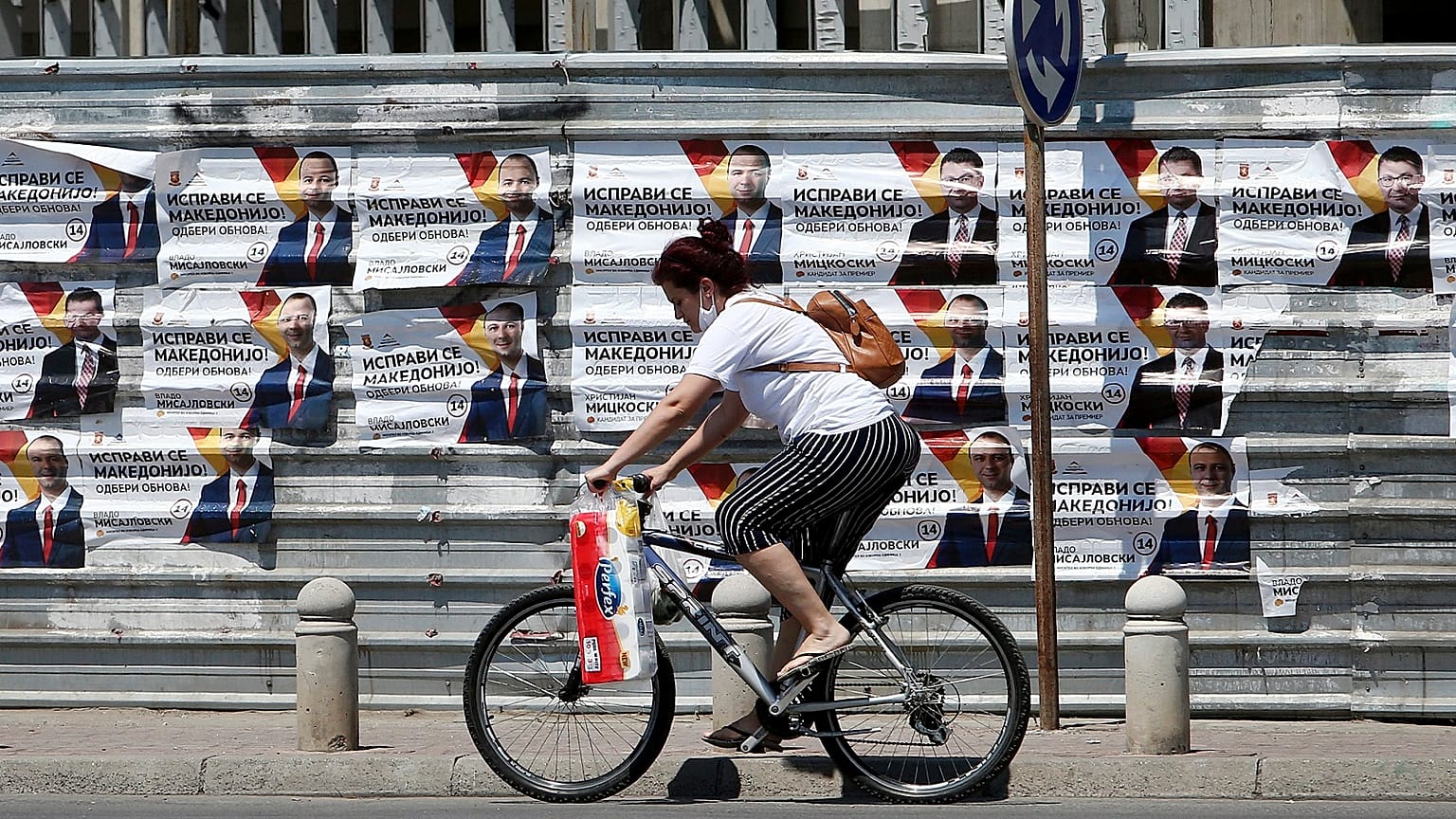 A woman rides a bicycle past electoral campaign posters of the largest opposition party VMRO-DPMNE