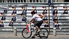 A woman rides a bicycle past electoral campaign posters of the largest opposition party VMRO-DPMNE