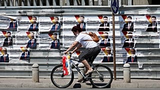 A woman rides a bicycle past electoral campaign posters of the largest opposition party VMRO-DPMNE