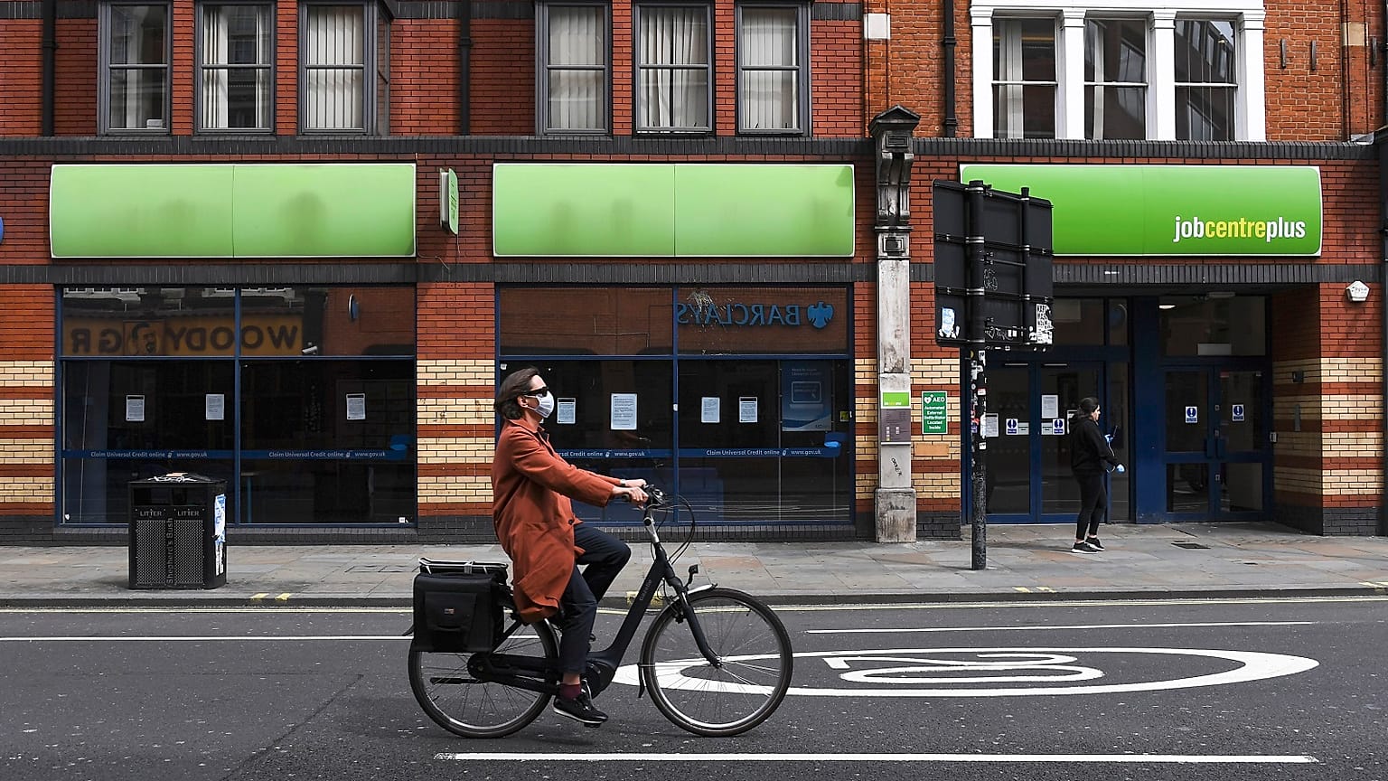 A woman wearing a mask rides a bicycle past a job centre in Shepherd's Bush, London.