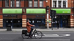 A woman wearing a mask rides a bicycle past a job centre in Shepherd's Bush, London.