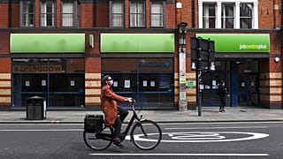 A woman wearing a mask rides a bicycle past a job centre in Shepherd's Bush, London.