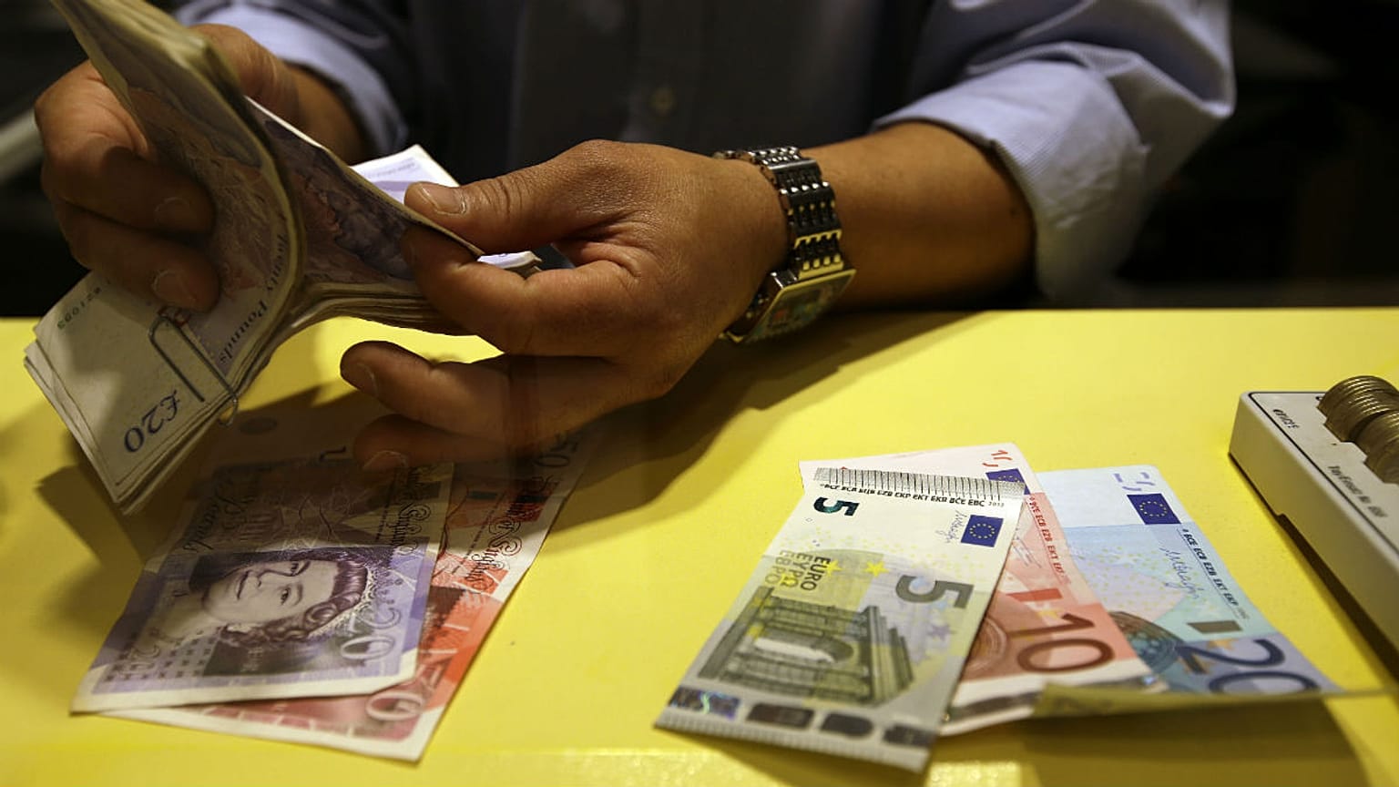 An employee counts British pounds and Euro notes at a currency exchange office