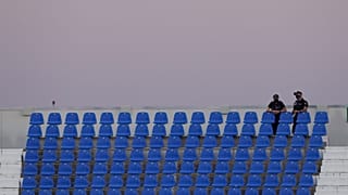 Gradas de un campo de fútbol sin aficionados y policías vigilando con mascarilla