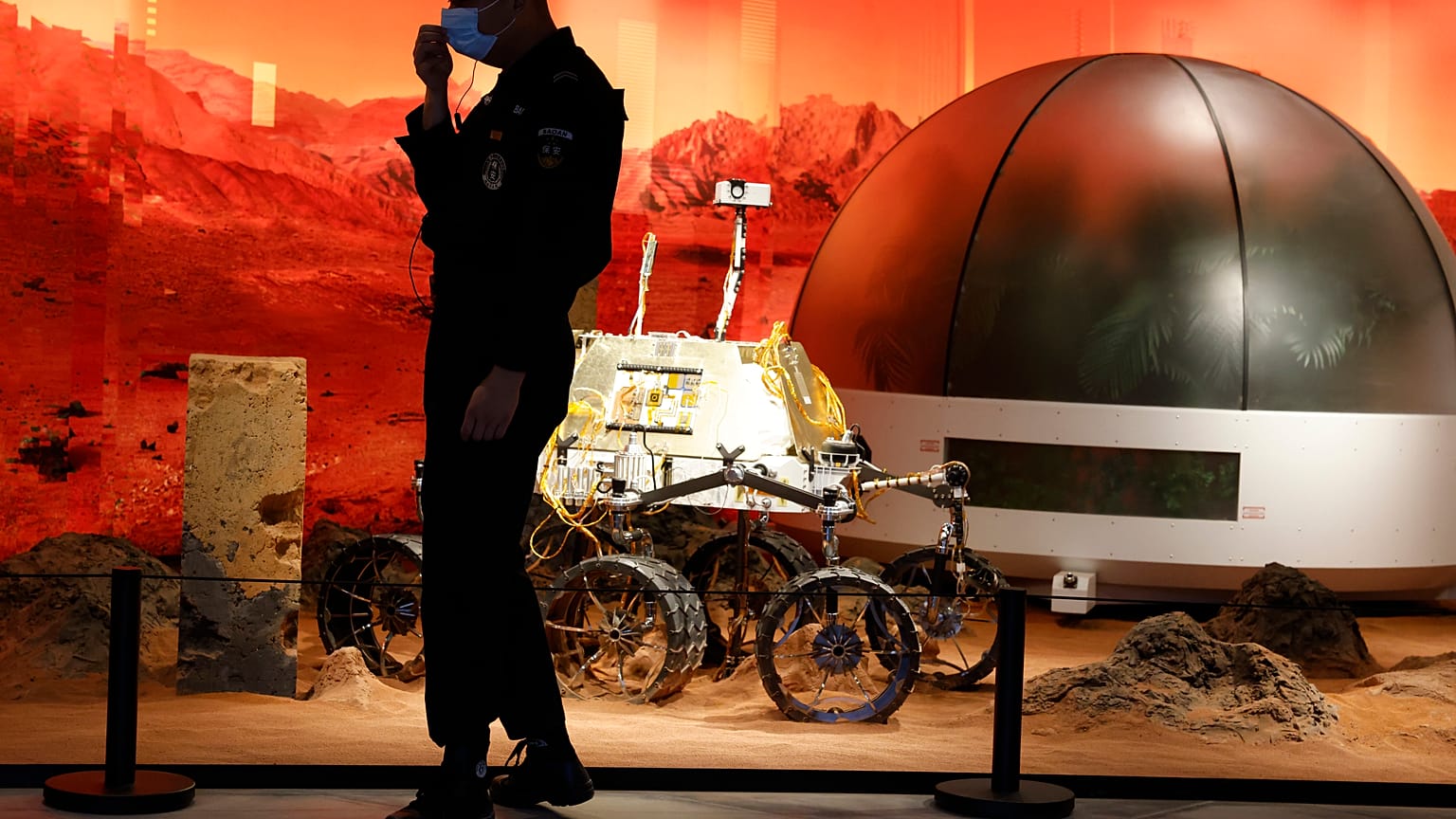 A security guard adjusts his mask near an exhibition of rovers and bio-domes on Mars in Beijing Thursday, July 23, 2020. 