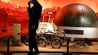 A security guard adjusts his mask near an exhibition of rovers and bio-domes on Mars in Beijing Thursday, July 23, 2020. 