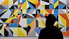 A man passes a colorful tiled mural by American artist Sarah Morris in the old town of Duesseldorf, Germany, Tuesday, July 14, 2020.