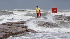 Galveston Island Beach Patrol lifeguard Matthew Herdrich walks along rocks as waves kicked up by Tropical Storm Hanna wash over them.