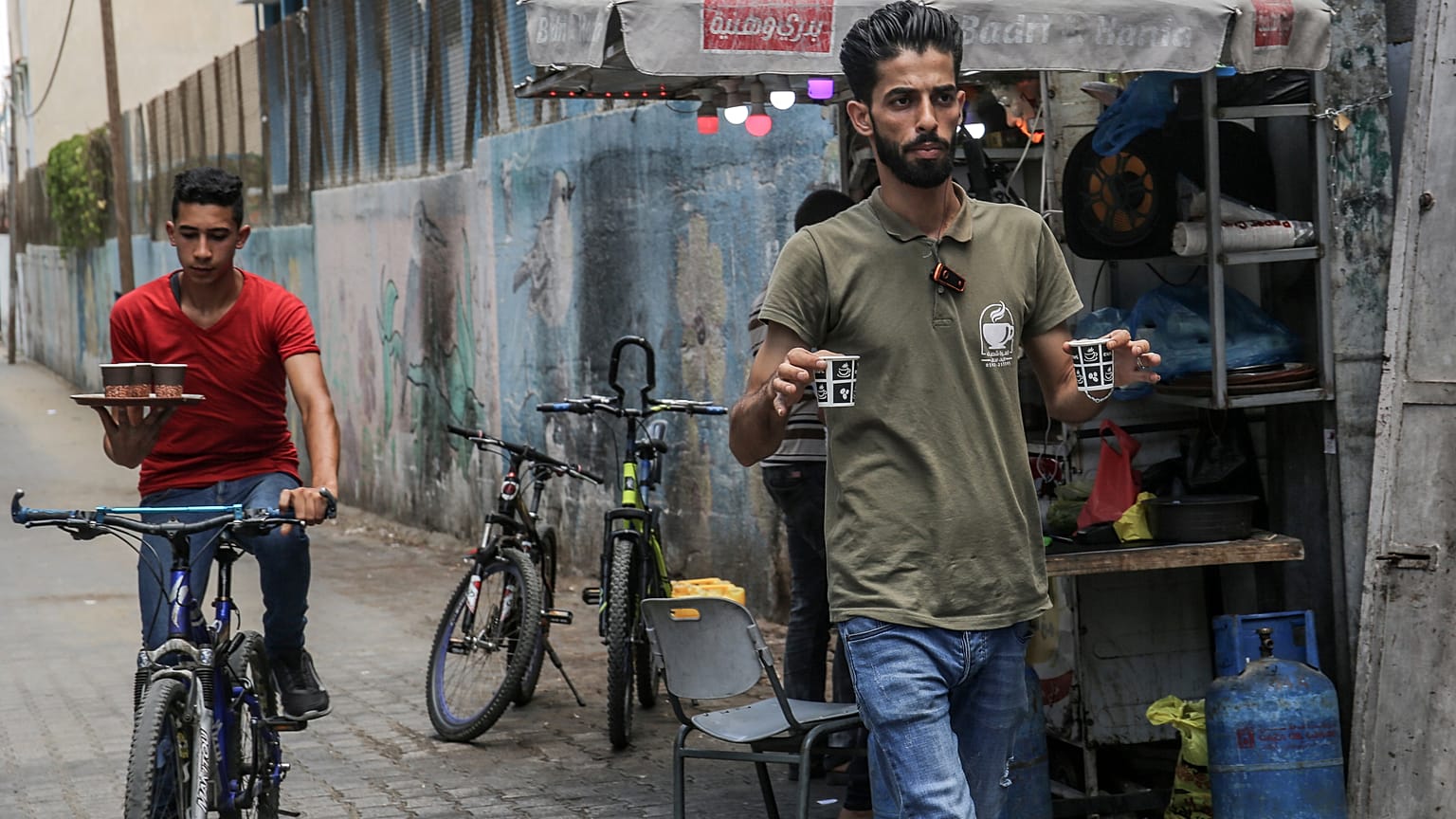 شعبان حمودة (يمين) حاملاً فنجانيْ قهوة بينما يتحضر أحد موظفيه إلى الانطلاق على دراجته الهوائية لخدمة زبائن 