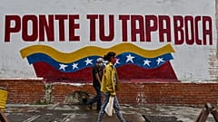 Venezolanos caminan en Caracas ante un cartel que invita a ponerse la mascarilla