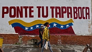 Venezolanos caminan en Caracas ante un cartel que invita a ponerse la mascarilla