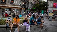 People wearing face masks to prevent the spread of coronavirus, sit on a bench street in downtown Madrid, Spain, Tuesday, July 28, 2020. 
