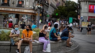People wearing face masks to prevent the spread of coronavirus, sit on a bench street in downtown Madrid, Spain, Tuesday, July 28, 2020. 