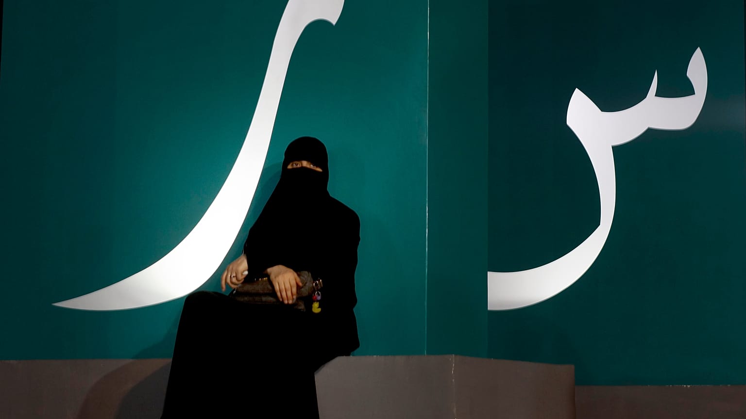 مرأة تجلس عند لافتة مكتوبة بحروف عربية خلال حدث ثقافي  حديقة الواجهة المائية بجدة/ المملكة العربية السعودية