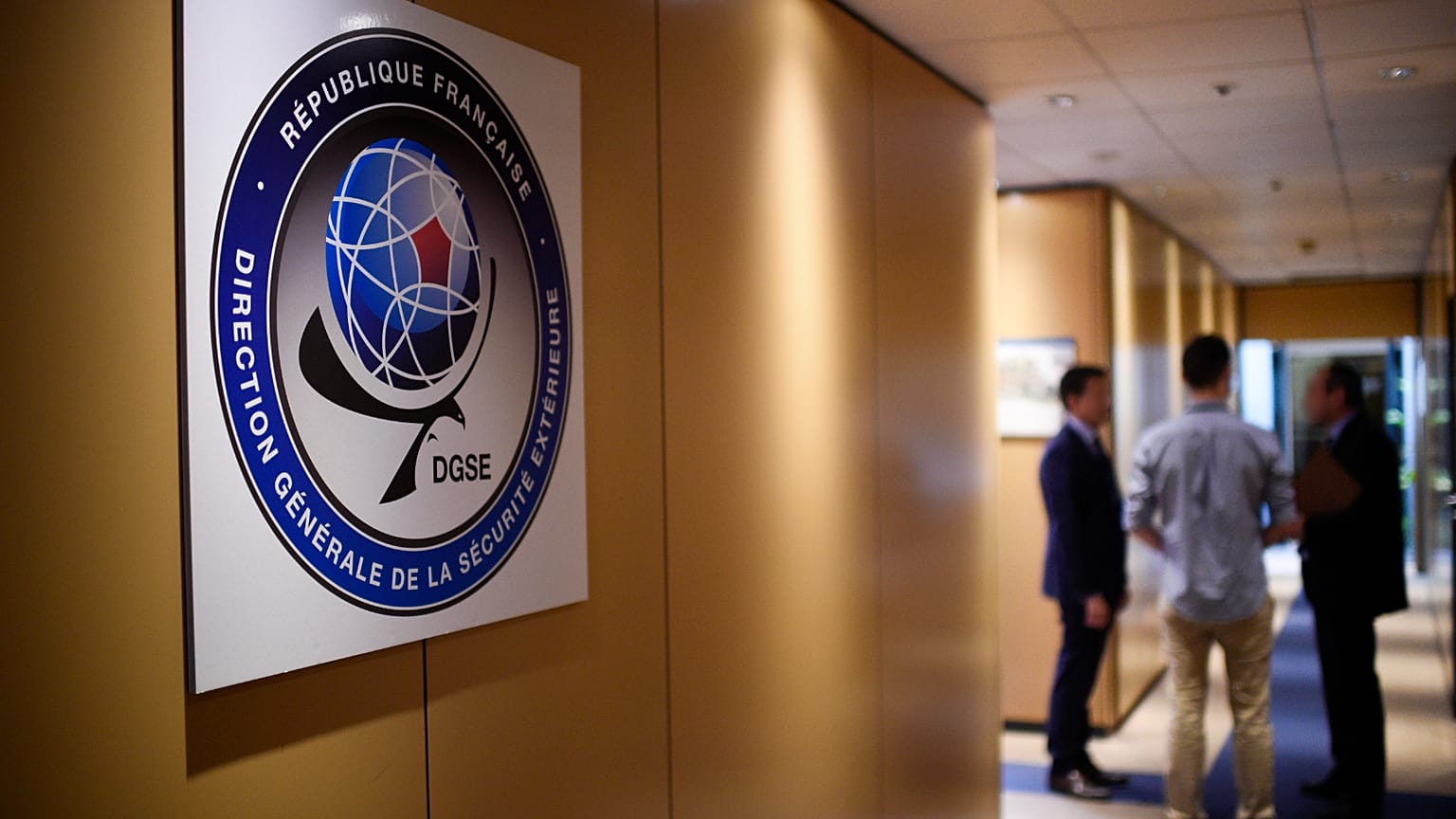Three men speak in a corridor at the headquarters of the General Directorate for External Security (DGSE)