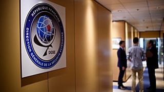 Three men speak in a corridor at the headquarters of the General Directorate for External Security (DGSE)