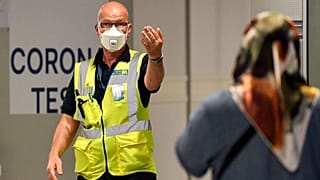 Duesseldorf Havaalanı'na gelen yolcuları, Covid-19 test merkezine yönlendiren bir görevli