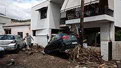 A woman walks between damaged cars following a storm at the village of Politika, on Evia island, northeast of Athens