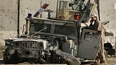 An Iraqi army soldier talks on his phone as he stands next to an army vehicle damaged in previous fighting, at an Iraqi army base in Sukor neighborhood