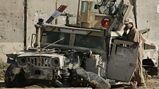 An Iraqi army soldier talks on his phone as he stands next to an army vehicle damaged in previous fighting, at an Iraqi army base in Sukor neighborhood