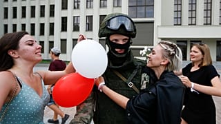 Mujeres abrazan a un soldado que vigila el edificio del Gobierno en Minsk en una protesta pacífica conra la represión policial