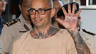 Artur Segarra Princep de España levanta la mano mostrando un popular verso de la Biblia en la palma de la misma leyendo, "Lucas 23:34" al llegar al tribunal penal de Bangkok, 