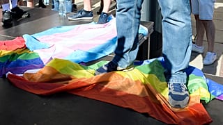 A man stands on a Rainbow Flag as he attends a demonstration of far-right activists against LGBT rights in Warsaw, Poland, Sunday, Aug. 16, 2020.