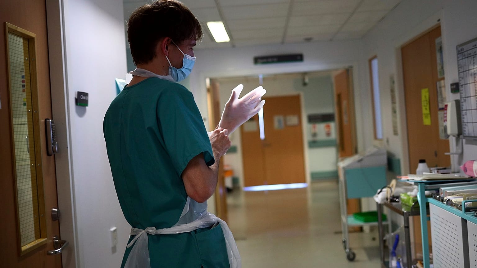 A junior doctor dons PPE to visit a patient.