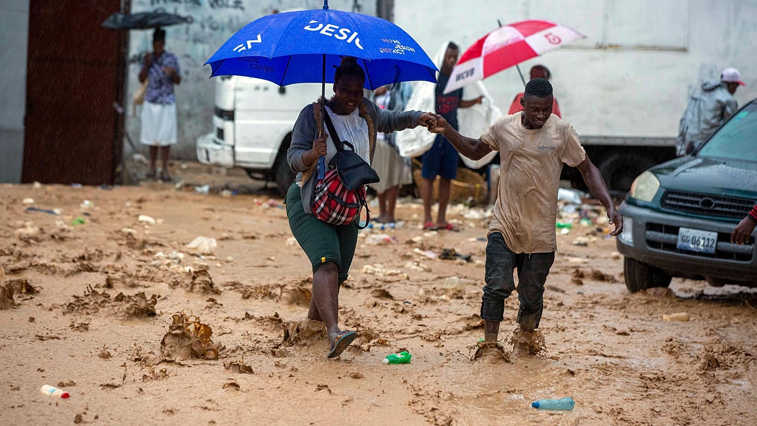 A woman is helped by a man to cross a flooded street during the passing of Tropical Storm Laura in Port-au-Prince, Haiti, Sunday, Aug. 23, 2020.