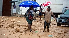 A woman is helped by a man to cross a flooded street during the passing of Tropical Storm Laura in Port-au-Prince, Haiti, Sunday, Aug. 23, 2020.