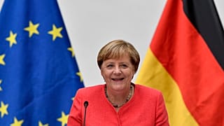 FILE: German chancellor Angela Merkel sits between a European and a German flag in Duesseldorf, Germany, Tuesday, Aug. 18, 2020. 