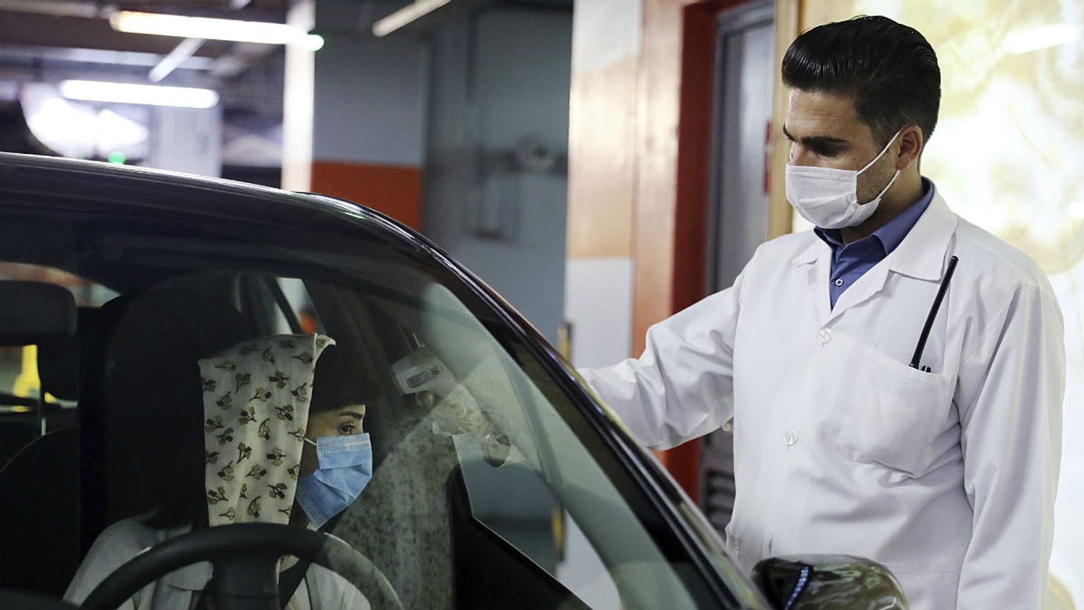 A woman wearing a protective face mask to help prevent spread of the coronavirus has her temperature checked as she enters a shopping center, in Tehran, Iran