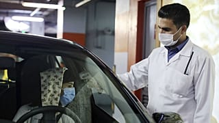 A woman wearing a protective face mask to help prevent spread of the coronavirus has her temperature checked as she enters a shopping center, in Tehran, Iran