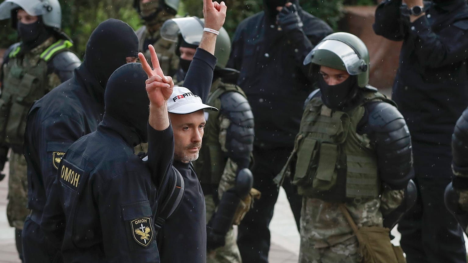 A man makes v-signs in front of a riot police blockade as he is detained during a protest at the Independence Square in Minsk, Belarus, Thursday, Aug. 27, 2020.