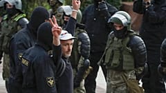 A man makes v-signs in front of a riot police blockade as he is detained during a protest at the Independence Square in Minsk, Belarus, Thursday, Aug. 27, 2020.
