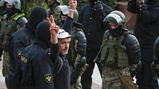 A man makes v-signs in front of a riot police blockade as he is detained during a protest at the Independence Square in Minsk, Belarus, Thursday, Aug. 27, 2020.