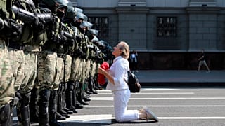 Una donna si inginocchia davanti agli agenti della polizia antisommossa, che blocca la manifestazione dei sostenitori dell'opposizione bielorussa, Minsk