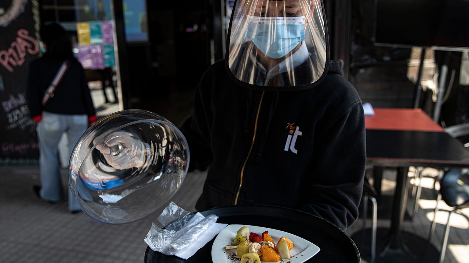 Un camarero con mascarilla y visera de protección sirve un plato en Santiago de Chile