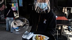 Un camarero con mascarilla y visera de protección sirve un plato en Santiago de Chile