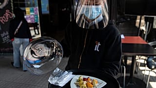 Un camarero con mascarilla y visera de protección sirve un plato en Santiago de Chile