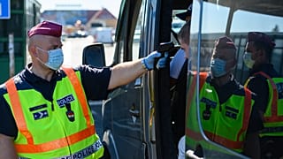Egy belépő gépjármű utasainak testhőmérsékletét ellenőrzi egy rendőrök a hegyeshalmi határátkelőnél 2020. szeptember 5-én. 