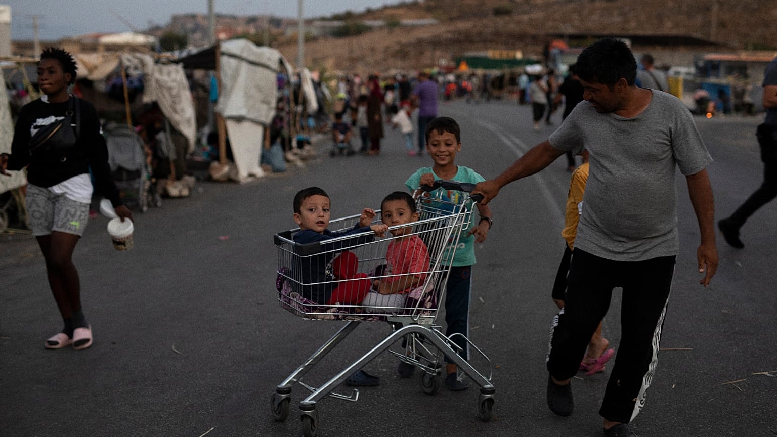 Two children sit inside a supermarket trolley as a migrant pulls them on the road near Mytilene town, on the northeastern island of Lesbos, Greece, Sunday, Sept. 13, 2020. 