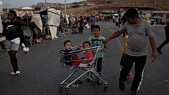 Two children sit inside a supermarket trolley as a migrant pulls them on the road near Mytilene town, on the northeastern island of Lesbos, Greece, Sunday, Sept. 13, 2020. 