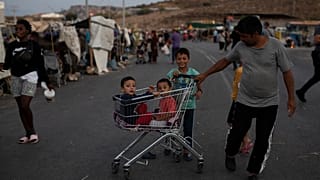 Two children sit inside a supermarket trolley as a migrant pulls them on the road near Mytilene town, on the northeastern island of Lesbos, Greece, Sunday, Sept. 13, 2020. 