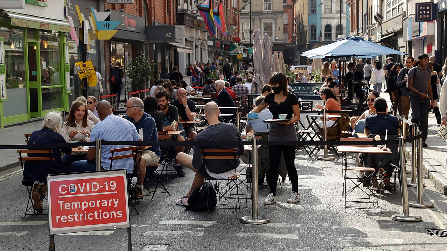 People sit outside on a street closed to traffic to try to reduce the spread of coronavirus in London, Saturday, Sept. 19, 2020.