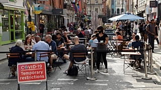 People sit outside on a street closed to traffic to try to reduce the spread of coronavirus in London, Saturday, Sept. 19, 2020.