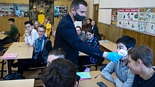 Преподаватель измеряет температуру ученику в московской школе.